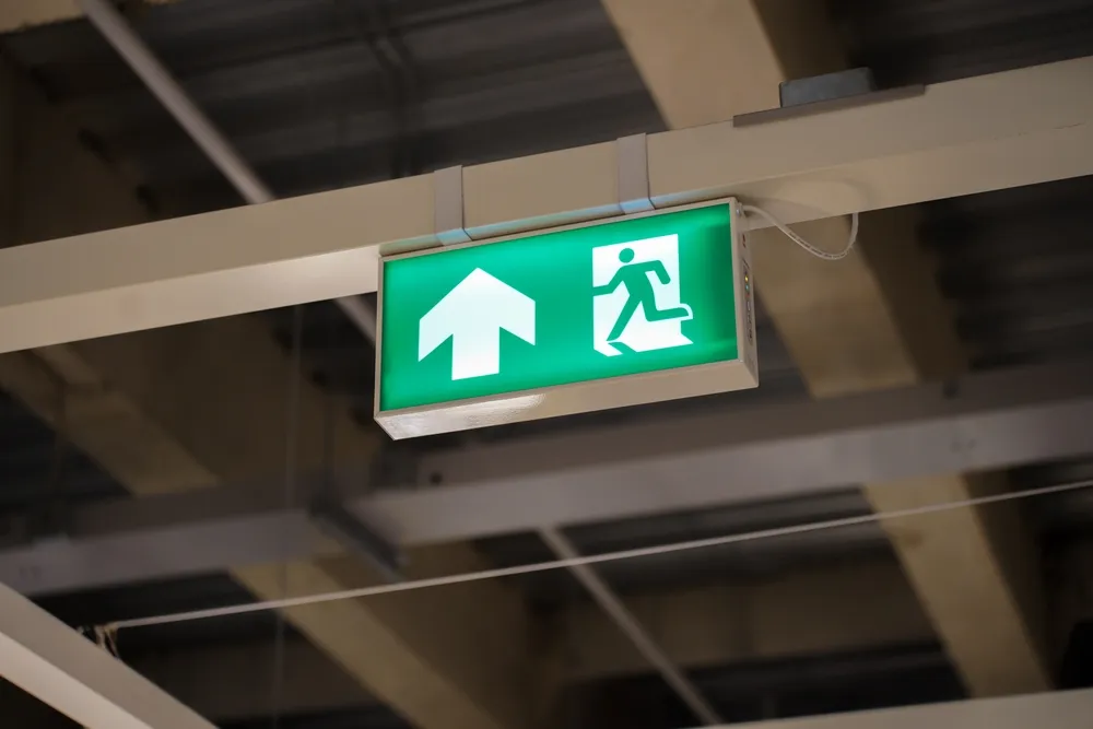 Verlicht groen ontruimingsbord met vluchtroutepictogram en pijl omhoog voor evacuatie tijdens een noodsituatie.