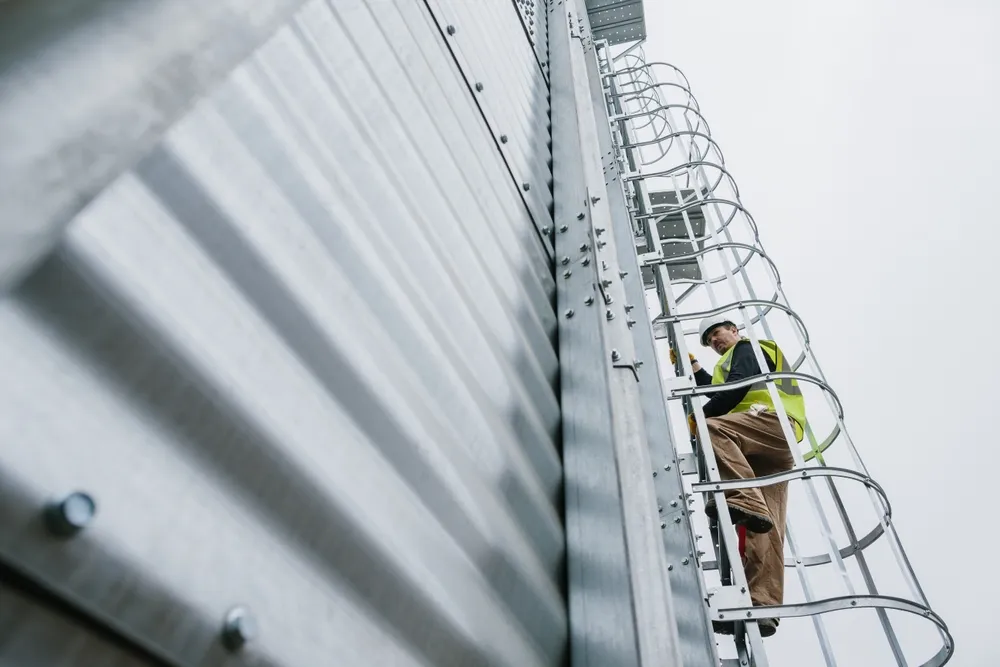 "alleenwerker met veiligheidsvest klimt een vaste ladder op langs de buitenkant van een industriële installatie."
