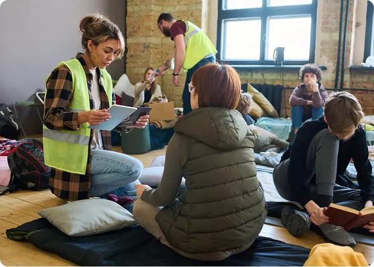 Foto einer freiwilligen Helferin, die Menschen in einer Flüchtlingsunterkunft führt  